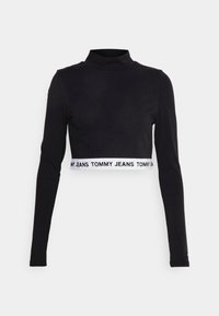 Black long-sleeve crop top with a mock neck. Features a white elastic band with ‘TOMMY JEANS’ text at the hem. Made of stretch fabric.