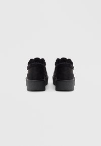 Des chaussures à plateforme en suedine noire avec une semelle en caoutchouc texturée noire. L'arrière présente une finition douce et moelleuse le long du col.