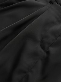 Svart tyg med en slät textur, veck och en dold sidoficka, som visar detaljerad sömnad och en platt midjeband.