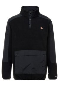 Chaqueta tipo pulóver negra con cuello alto, confeccionada en material de forro polar y detalles de nylon. Incluye una tapeta con botones en la parte frontal y un bolsillo delantero.