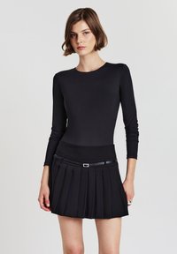 Maglietta nera a maniche lunghe abbinata a una gonna nera plissettata con un cintura a contrasto e un sottile accentuato da una cintura. Tessuto morbido e liscio.