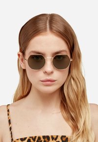 Osmerokutne sunčane naočale s metalnim okvirom i tamnim staklima. Okvir je tanak i zlatne boje, s jednostavnim dizajnom mosta.