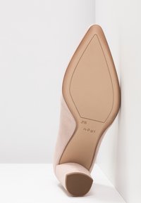 Chaussure à talon haut en suede nude avec un bout effilé et un talon carré, dotée d'une semelle texturée et d'un branding discret au bas.