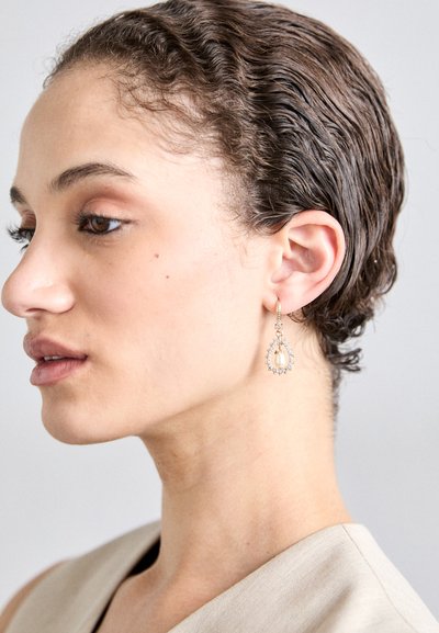 Guldtonede dråbeøreringe med en tårnformet perle omgivet af en cirkel af små klare sten, hængende elegant fra en hoops vedhæftning.