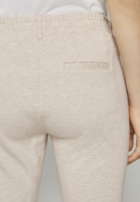 Beige sweatpants tillverkade av mjukt, texturerat tyg, med en elastisk midja och en enda bakficka med platt kant.