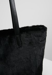 Černá taška z umělé kožešiny s elegantními černými koženými popruhy. Povrch vypadá jemně a strukturovaně, s jednoduchým a nezdobeným designem.