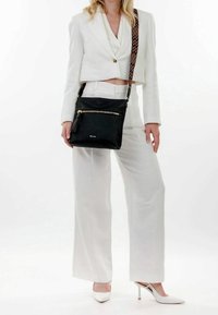 Borsa a tracolla nera in pelle con superficie testurizzata, dettagli in zip dorata e una tracolla decorata. Posizionata su uno sfondo chiaro.