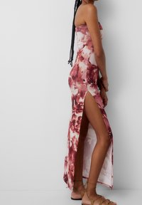 Robe maxi sans bretelles en tissu léger avec un motif floral dans des teintes de rose et de bordeaux, présentant une fente sur le côté et une silhouette ajustée.
