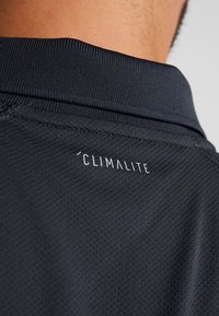 Gros plan sur la nuque d'un maillot de sport noir en tissu texturé avec le texte blanc "CLIMALITE" sous le col.