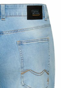 Lyseblå denimjeans bagpå med en syet lomme og et sort Camel Active mærke på taljebåndet.