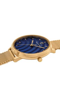 Guldtonad armbandsur med en strukturerad blå urtavla, guldiga timmarkörer och nätarmband. Har en krona och en subtil logotyp på urtavlan.