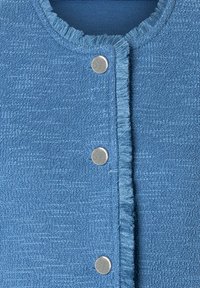 Cardigan bleu texturé avec un col à frange, cinq boutons-pression en métal brillant et une doublure intérieure douce de couleur contrastante.