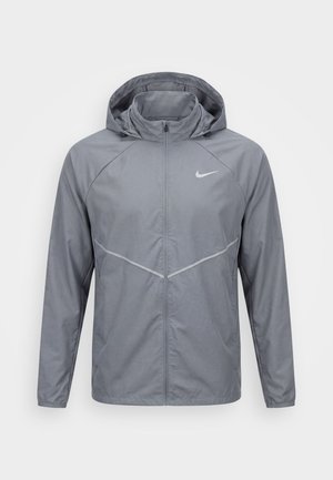Veste légère grise pour homme avec capuche, fermeture éclair intégrale à l'avant et logo Nike sur la poitrine, conçue pour une utilisation extérieure.