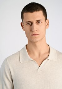 Ljus beige tröja med mjuk textur, V-ringning och en subtil polo-krage. Tyget ser slätt och bekvämt ut, perfekt för avslappnad klädsel.