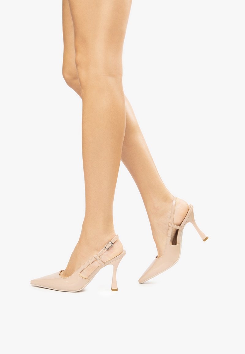 Nude lakierowane sandały na obcasie typu slingback z ostrym czubkiem, cienkim obcasem w szpilkę oraz paskiem w kostkę z małym zapięciem.