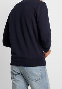 Felpa a girocollo blu navy realizzata in tessuto morbido, con maniche lunghe, polsini a costine e una vestibilità comoda. Dettaglio di cucitura visibile all'orlo.