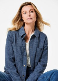 Blue textured jacket with a collar, two front pockets, and snap buttons, worn over a white shirt. The fabric appears woven and soft.