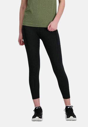 Schwarze Leggings aus dehnbarem Stoff, mit einer taillierten Passform und seitlichen Taschen, kombiniert mit einem grünen T-Shirt mit kurzen Ärmeln und schwarzen Turnschuhen.
