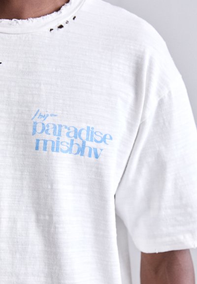Valge lühikeste varrukatega t-särk, millel on veidi tekstuuriga kangas. Ees on sinine graafiline tekstidisain, kus on kirjutatud " /by/ paradise misbhv".