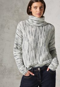 Gehaakte pullovertrui in wit en zwart met een coltrui-ontwerp. Kenmerkt zich door een gestructureerd patroon en geribde manchetten. Gecombineerd met donkere denim jeans.