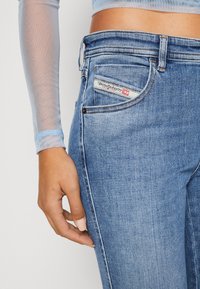 Jeans de denim azul claro con un ajusteSlim. Presentan un bolsillo trasero cosido con una etiqueta de logo, costuras en contraste y una cintura de altura media.