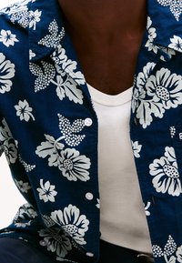 Navy blue floral shirt with white patterns, featuring a button-down front and short sleeves, layered over a plain white t-shirt.