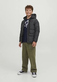 Čierna nadýchaná bunda s kapucňou, na zips vpredu a s dvoma prednými vreckami, oblečená cez námorníckonosú mikinu a široké olivovo zelené nohavice. Čierne tenisky.