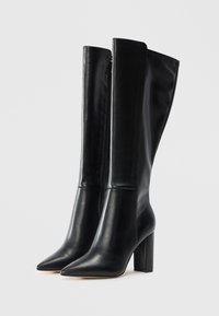Black knee-high leather boots with pointed toes and block heels, standing side by side on a plain white background.