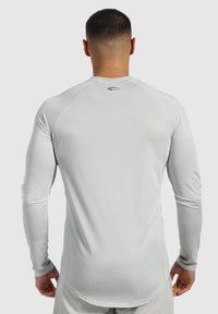 Hellgraues, langärmliges Sportshirt aus strukturiertem Stoff, mit Raglanärmeln und einem dezenten Logo auf der Rückseite.