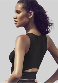 Schwarzes ärmelloses Crop-Top mit enganliegendem Design und einem offenen Rückenausschnitt. Die glatte Textur und der minimalistische Stil ergänzen die Silhouette.