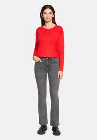 Czerwona sweter z długim rękawem i okrągłym dekoltem, z regulowanymi sznurowadłami, zestawiony z szarymi dżinsami w stylu dzwonów i czarnymi botkami na platformie.