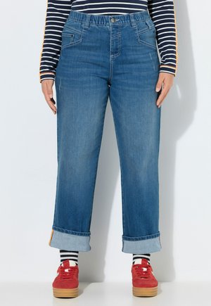 Person iført opsmøgede blå jeans, navy- og hvidstribet langærmet skjorte, sort- og hvidstribede strømper og røde platform-sneakers.