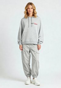 Hoodie grigio con la scritta "SWEET heart" ricamata in rosso, abbinato a pantaloni cargo grigi chiari con tasche laterali e sneakers bianche.