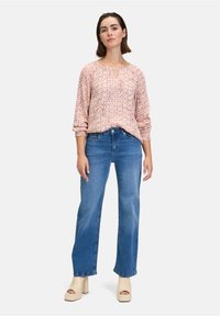 Blusa a fiori di colore rosa chiaro con scollatura a V, abbinata a jeans blu a gamba dritta e tacchi alti beige.