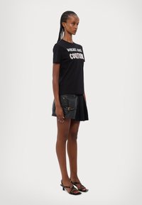Must musta T-särk, millel on valgete tähtedega "Versace" ja "Couture", koos musta nahast mini-seelikuga, millel on kuldsed aktsendid ja keha lähedane disain.