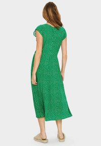 Vihreä midi mekko lyhyillä hihoilla, valkoisilla pilkuilla ja rentolla leikkauksella. Kevyestä kankaasta valmistettu, jossa on hienovarainen tekstuuri ja sivuaukot.