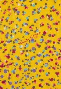 Tessuto con uno sfondo giallo brillante, caratterizzato da un motivo sparso di macchie colorate in blu, viola, rosso e marrone. "Manila Grace" stampato in rosso.