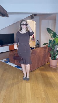 Robe cintrée marron avec des manches trois-quarts, une ceinture à la taille et un ourlet à volants. Associée à un petit sac à main marron et des lunettes de soleil.
