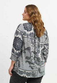 Grå bluse med indviklede sorte paisley- og blomster mønstre, lange ærmer med indsamlede manchetter og en løs pasform.