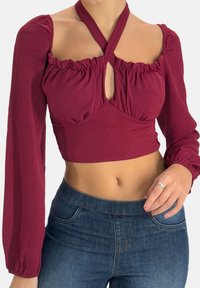 Vinröd croppad topp med puffärm, rynkad halsringning och ett nyckelhålsutskärning i mitten, kombinerad med högmidjade blå jeans.