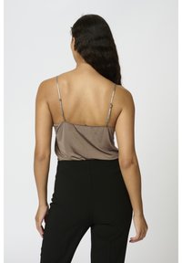 Musta satiininen toppi ohuilla olkaimilla, yhdistetty korkeavyötäröisiin mustiin housuihin. Topissa on sileä pinta ja valuva muotoilu.