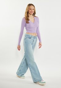 Cardigan cropped a coste di colore viola chiaro con bottoni, abbinato a jeans a vita alta blu chiaro con gamba larga e sneakers multicolori.