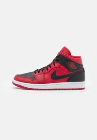 Rode en zwarte mid-top Air Jordan sneaker met zwarte veters, witte zool en logo op de kraag tegen een witte achtergrond.