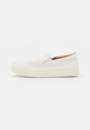 Baskets blanches slip-on avec semelle épaisse et doublure intérieure beige, design simple, photographiées de profil sur un fond uni.