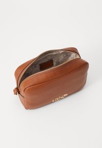 Borsa cosmetica in pelle marrone con bordi arrotondati, una zip dorata e dettaglio del logo. L'interno presenta una fodera a motivi.