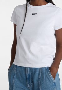 Witte katoenen t-shirt met ronde hals, korte mouwen en zwart "VANS" logo op de borst. Gecombineerd met losse blauwe denim broek.