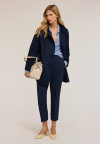 Námořnický vlněný dvouřadý kabát, světle modrý pletený top, šité námořnické kalhoty, béžová kabelka a světle žluté boty na blokovém podpatku.