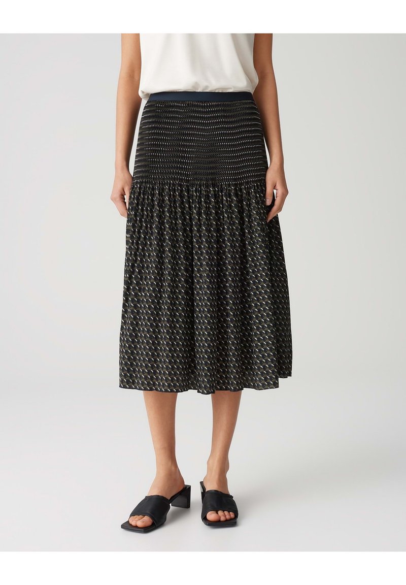 Jupe midi noire à motifs avec détail de taille froncée, fabriquée en tissu léger. Associée à des mules à talons carrés noires.