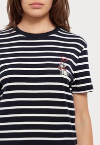 Námořnické a bílé pruhované bavlněné tričko s kulatým výstřihem a malým vyšitým designem psa se červeným srdíčkem nad ním.