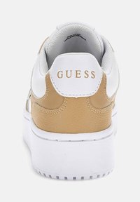 Sneaker bianco e beige con un tallone in pelle texturizzata, dotata di colletto imbottito e logo dorato "GUESS" sul retro. Suola spessa bianca.